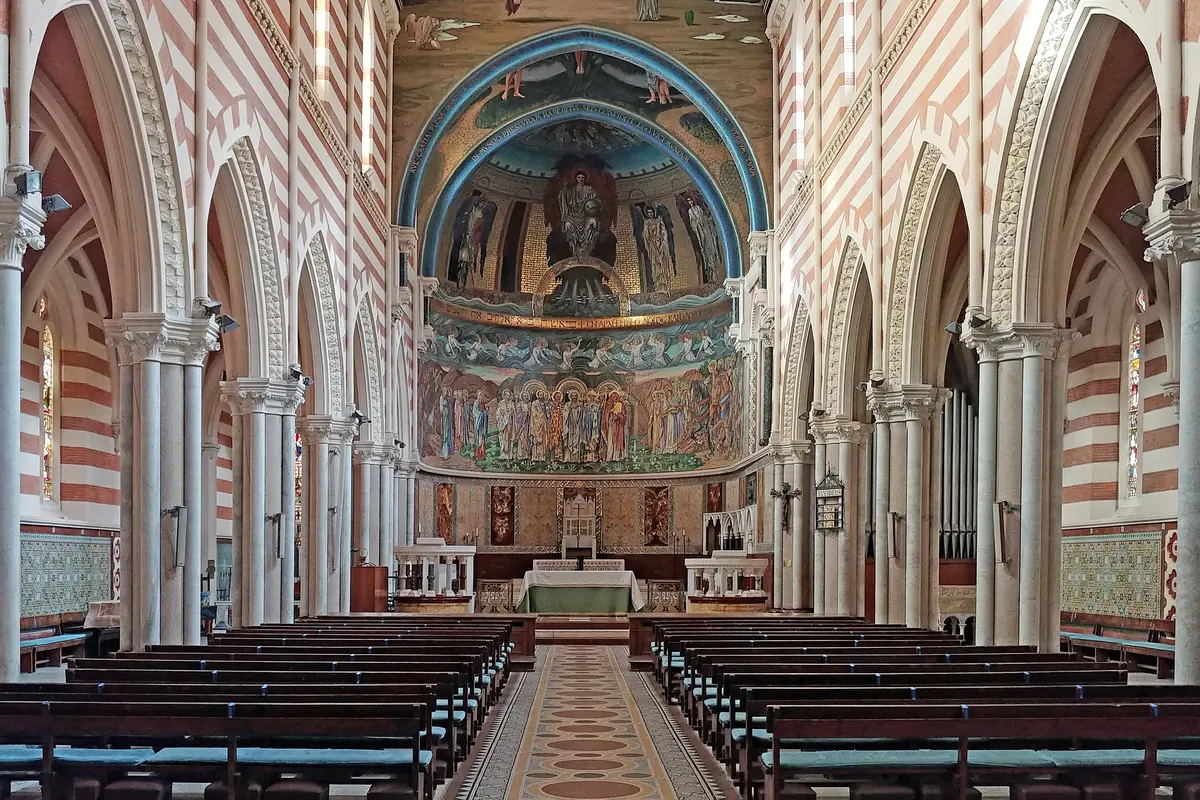 A view up the aisle from the back pews, past banded walls and a tiled floor to the mosaic apse.